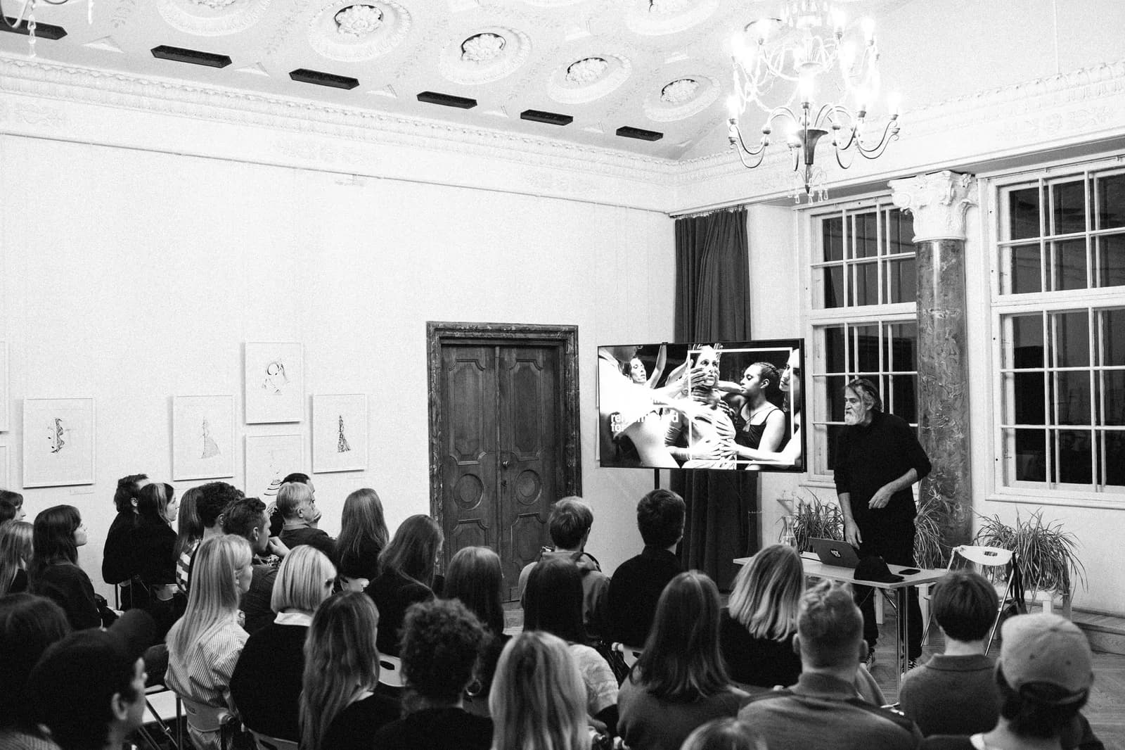 A speaker presenting beside a screen to a full audience.